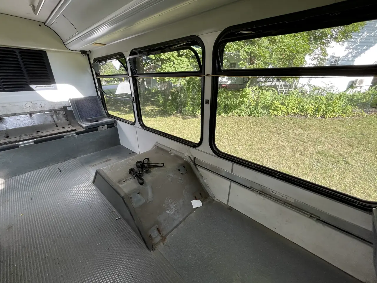 The cleared rear interior of the bus with open windows, bare floor and wall space waiting for shelving